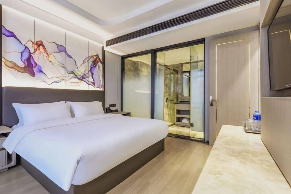 Una habitación de hotel moderna con una cama grande, un cristalero que da a un balcón y una obra de arte abstracta contemporánea en la pared.
