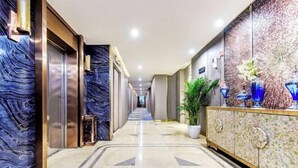 A hotel corridor with marble flooring, a decorative wall, and a cabinet with vases.