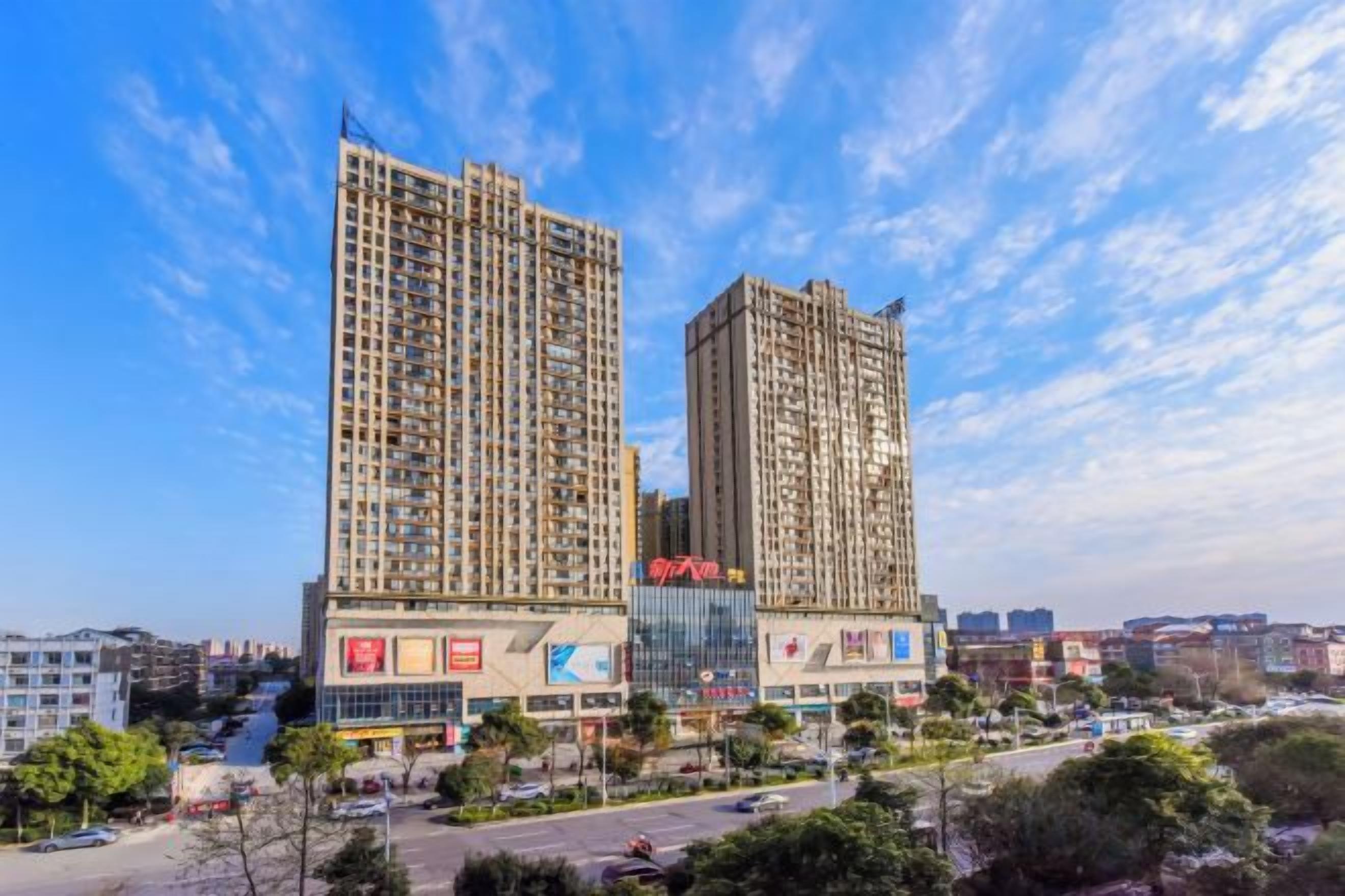 A high-rise building with multiple floors, surrounded by a parking lot and greenery.
