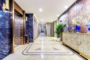 A hotel corridor with marble walls, a reception area with a decorative vase, and a potted plant.