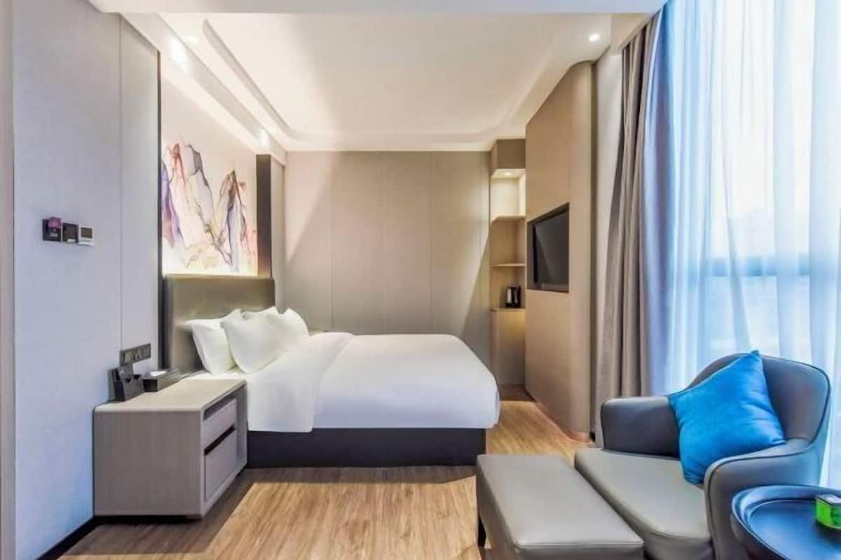 Una habitación de hotel moderna con una cama grande, una mesita de noche, una silla y un televisor de pantalla plana montado en la pared.