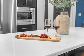 A marble countertop with a wooden board displaying food items and two wine glasses. - Panoramic Table Rock Lake Views with Hot Tub, Games & Free Branson Attraction Tickets (Hollister)