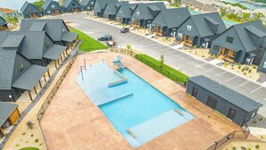 Zona residenziale con piscina, case dai tetti scuri e un parcheggio.