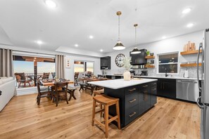 A modern kitchen with a central island, wooden flooring, and a dining area with a view. - Panoramic Table Rock Lake Views with Hot Tub, Games & Free Branson Attraction Tickets (Hollister)