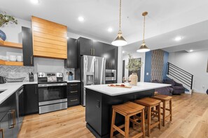 A modern kitchen with a central island, stainless steel appliances, and wooden bar stools. - Panoramic Table Rock Lake Views with Hot Tub, Games & Free Branson Attraction Tickets (Hollister)