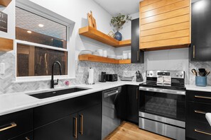 Uma cozinha moderna com armários pretos, lava-louças de aço inoxidável, forno duplo e janela com vista para a cidade.