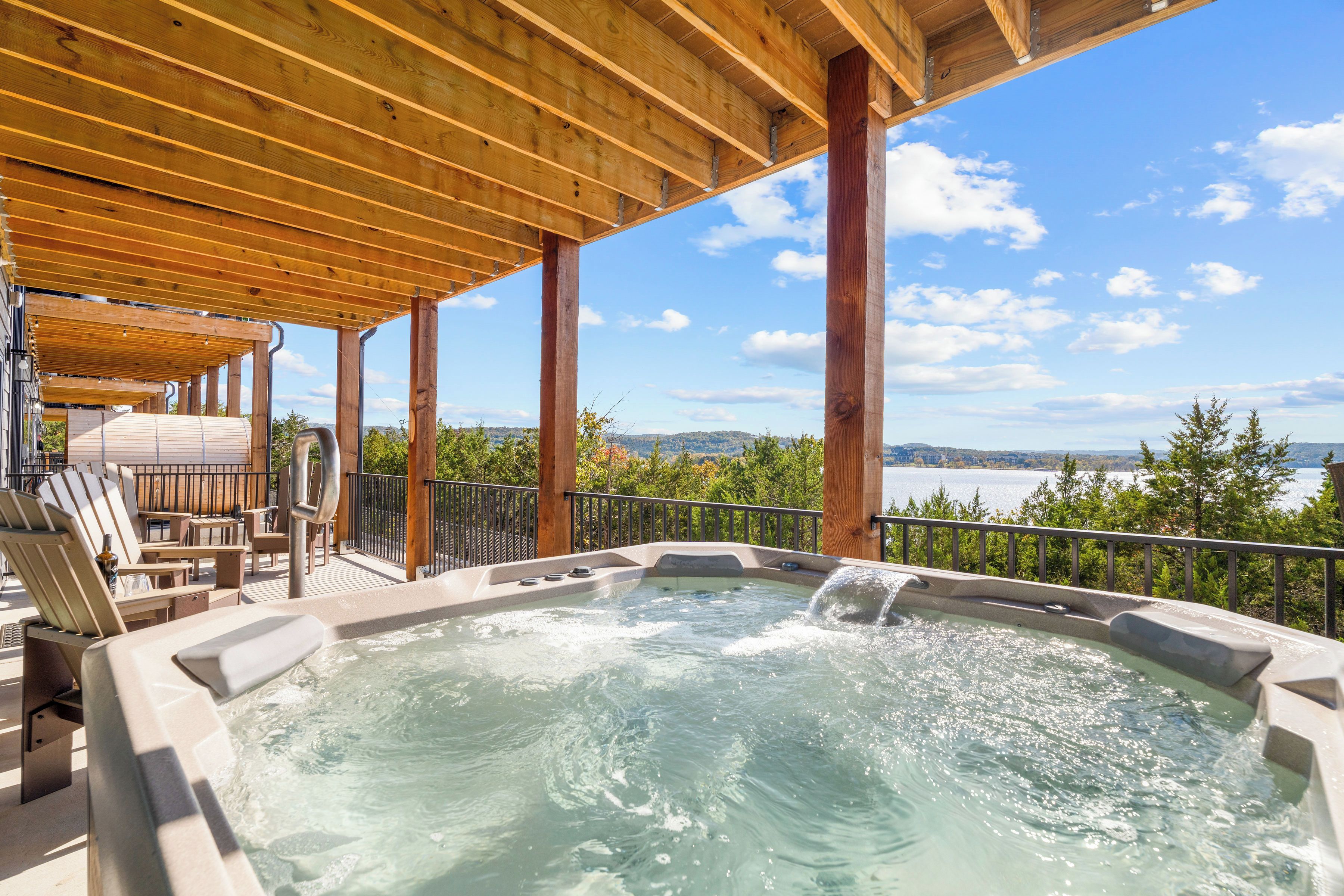 Un bain à remous avec une terrasse en bois et des chaises, offrant une vue sur un lac et des collines.