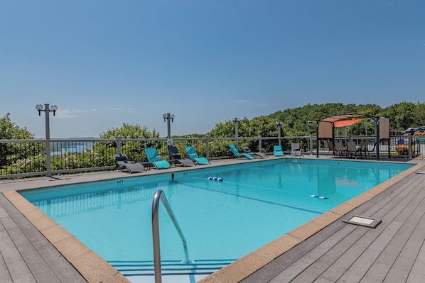 Ein rechteckiger Swimmingpool mit Holzterrasse, umgeben von Liegestühlen und einem Zaun.