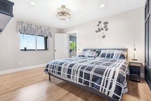 Ein Schlafzimmer mit einem großen Bett, einer Pendelleuchte, einem Fenster mit Blick und einer Tür zu einem weiteren Raum.