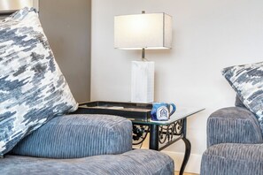A room with two grey upholstered chairs, a small table with a blue mug, and a white lamp on a stand.