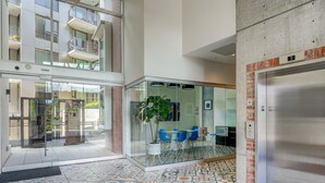 Eine moderne Lobby mit gemusterten Bodenfliesen, einer Glastrennwand, blauen Stühlen und einer Treppe zu einer oberen Ebene.