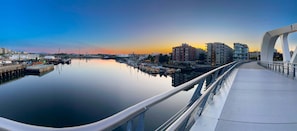 A waterfront view with a bridge, calm water, and buildings in the background.
