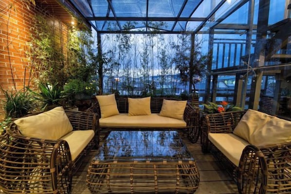 Un patio con paredes de vidrio, mobiliario de mimbre y una mesa de cristal.