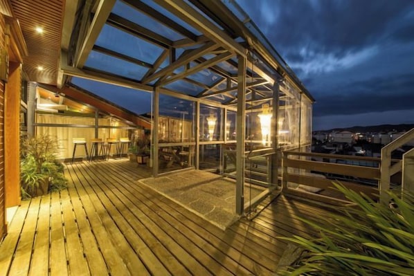 A covered outdoor area with a wooden deck, glass enclosure, and a view of the city at dusk. - Chengli Chengwai Inn (Lijiang)