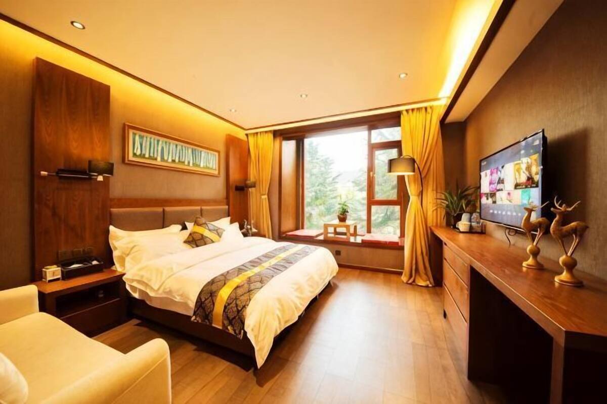 A hotel room with a large bed, a desk, a TV, and a window with curtains.