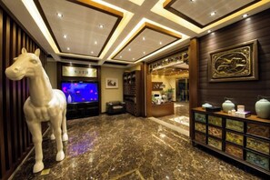 A lobby with a marble floor, a white horse statue, a television, and a decorative wall with a framed picture. - Chengli Chengwai Inn (Lijiang)