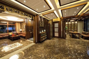 Un hall de hotel con piso de mármol, una zona de estar con sofás, una mesa de comedor y una recepción.
