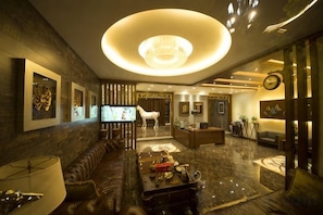 A modern hotel lobby with a large chandelier, leather seating, a television, and artwork on the walls.