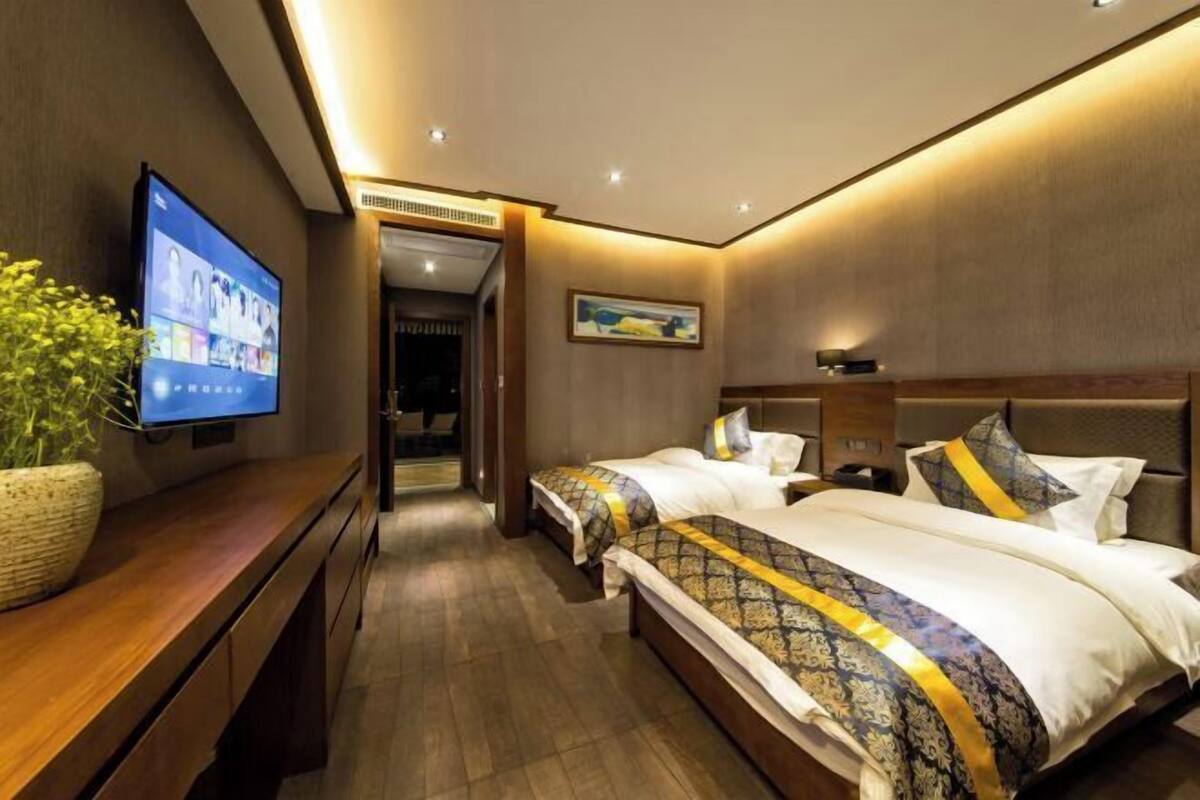 A hotel room with two beds, a TV on the left, a wooden desk, and a plant.