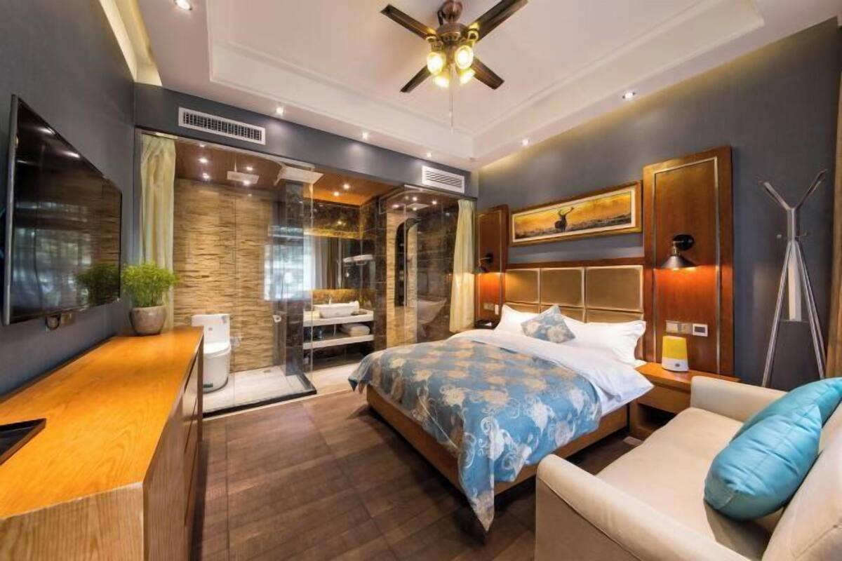 A modern hotel room with a large bed, a desk, a seating area, and a shower.