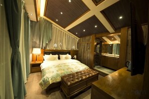 Une chambre à coucher avec un grand lit, un banc en bois, une table de chevet et une salle de bain visible à travers une porte ouverte.