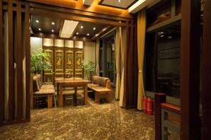 A room with a wooden dining table, chairs, a sofa, and a large window with curtains. - Chengli Chengwai Inn (Lijiang)