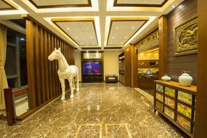 A hotel lobby with a marble floor, a white horse statue, a reception desk, and a wall with framed artwork. - Chengli Chengwai Inn (Lijiang)