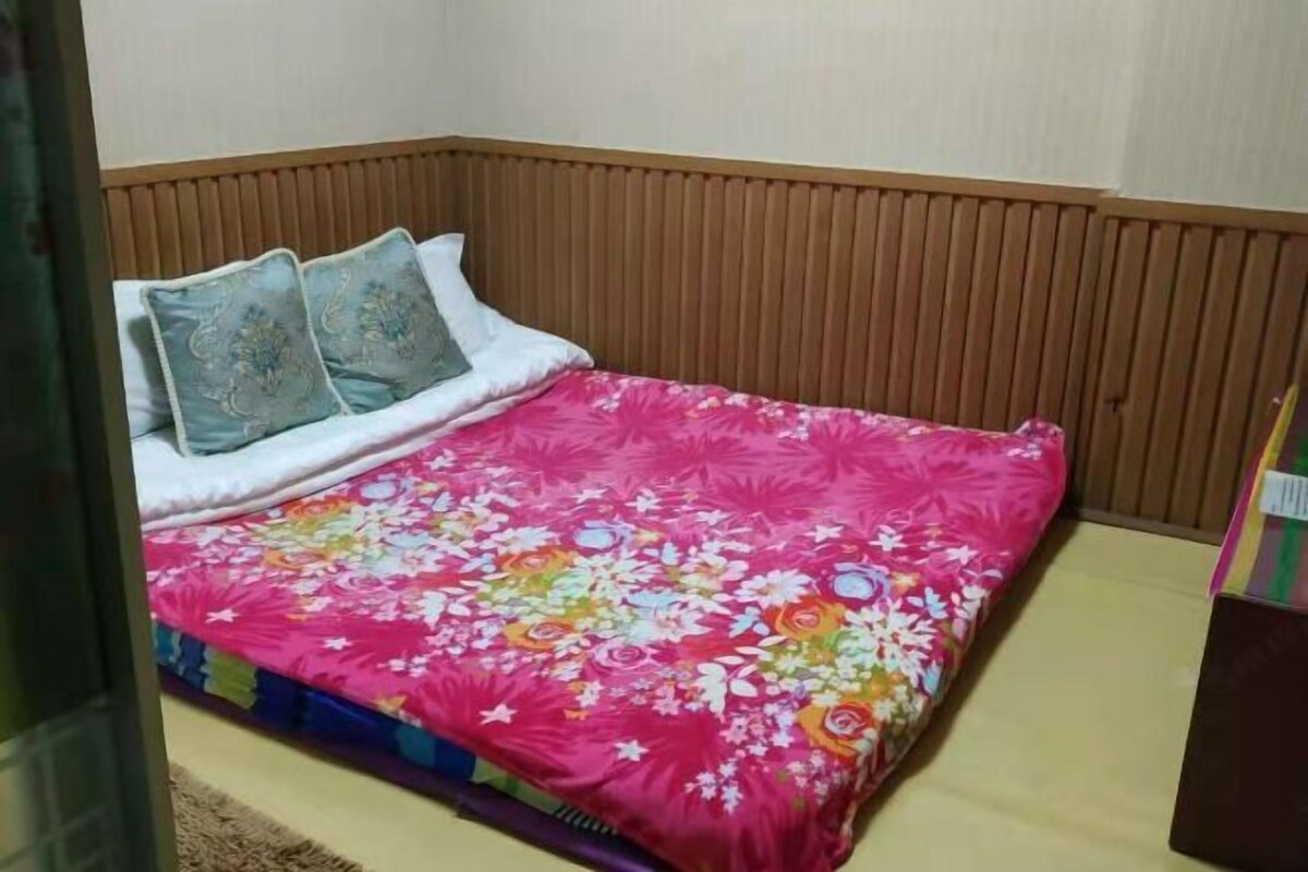 Una cama con una colcha estampada de flores y dos almohadas, un cabecero de madera y una mesita de noche pequeña.