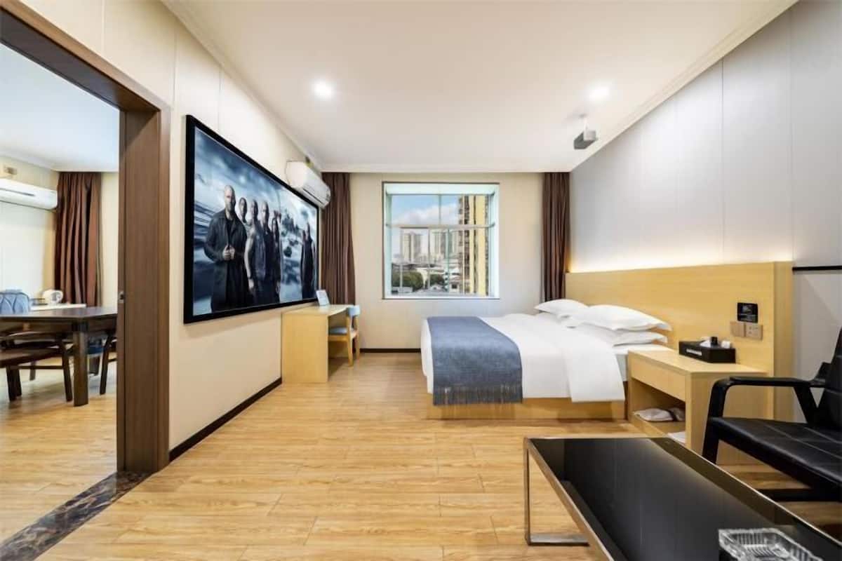 A hotel room with a bed, a desk, a chair, a TV, and a window with a city view.