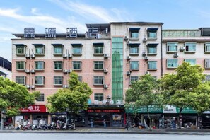A multi-story hotel with a central green facade, multiple balconies, and several ground-level shops. - Xinyuan Hotel (Xiushan Bus Terminal) (Xiushan County)
