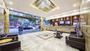A hotel lobby with a reception desk, seating area, and a large window overlooking the street.