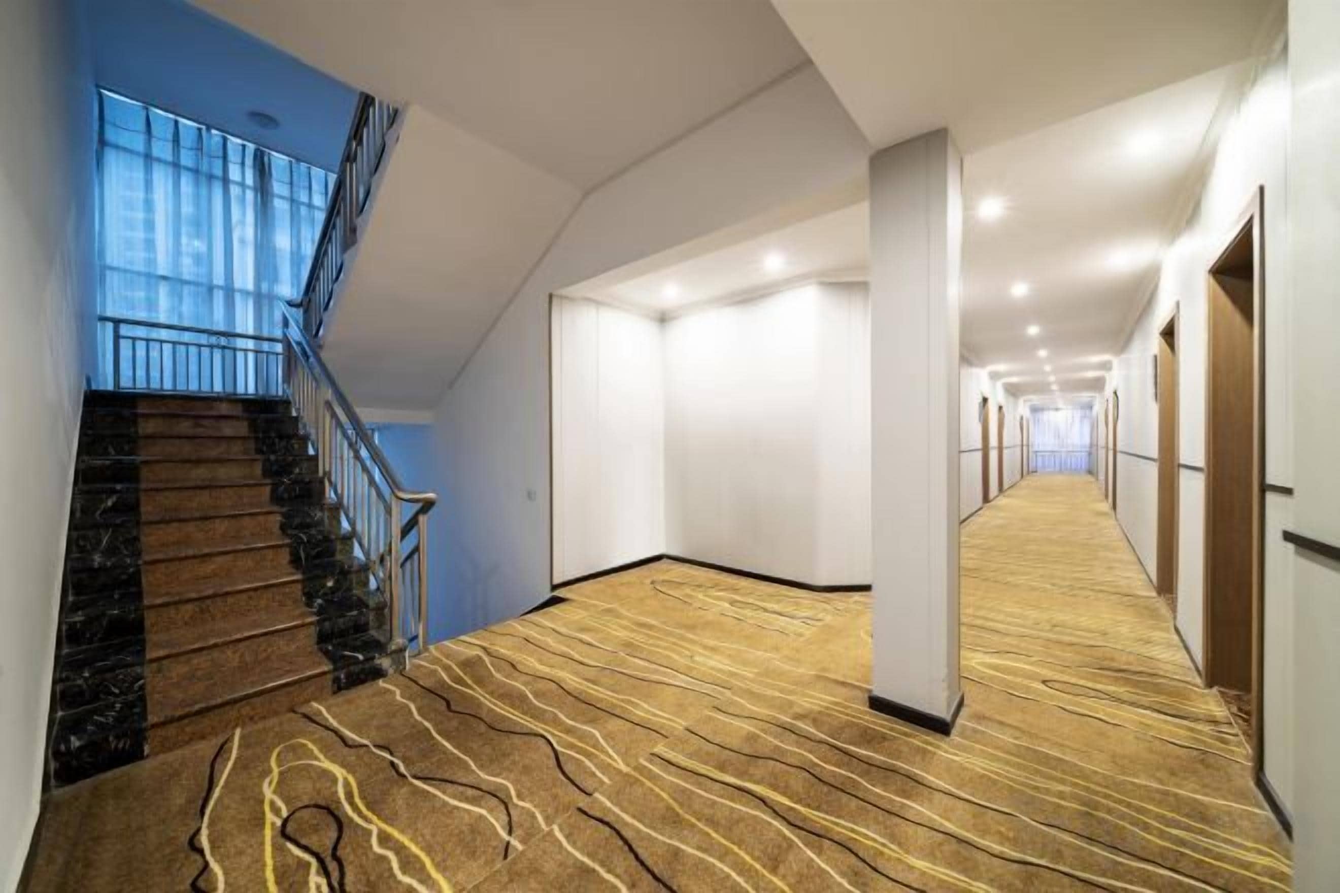 A hotel corridor with a carpeted floor, a staircase, and a view of the sky.