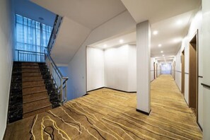 A hotel corridor with a carpeted floor, a staircase, and a view of the sky.