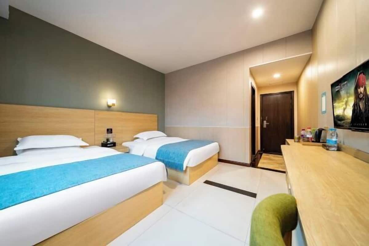 A hotel room with two beds, a desk, a chair, a nightstand, and a door leading to another room.