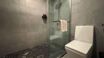 A modern bathroom with a glass-enclosed shower, a white toilet, and a tiled floor.