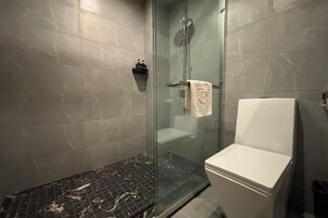 Um banheiro moderno com chuveiro em box de vidro, vaso sanitário branco e piso revestido de azulejos.