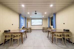Un salón de conferencias con pantalla de proyector, mesas y sillas.