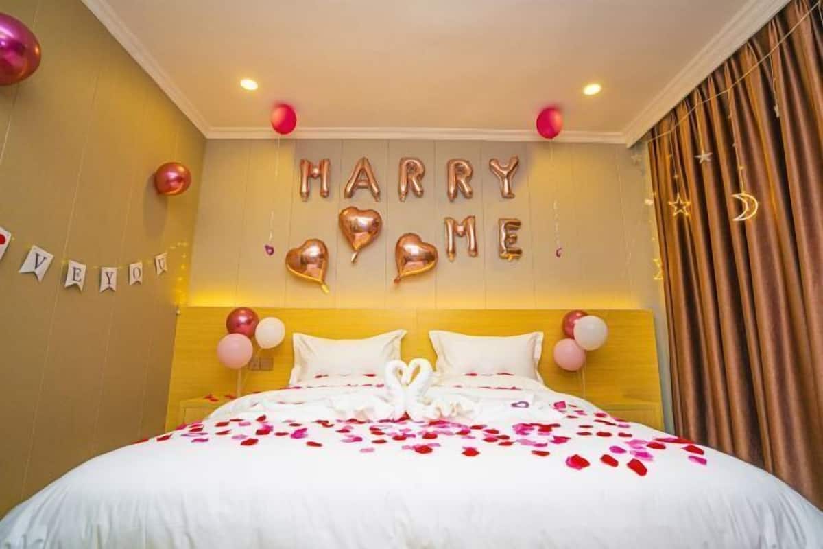 A hotel room with a bed, a wall with 'HAPPY BIRTHDAY' balloons, and a 'HAPPY BIRTHDAY' sign.
