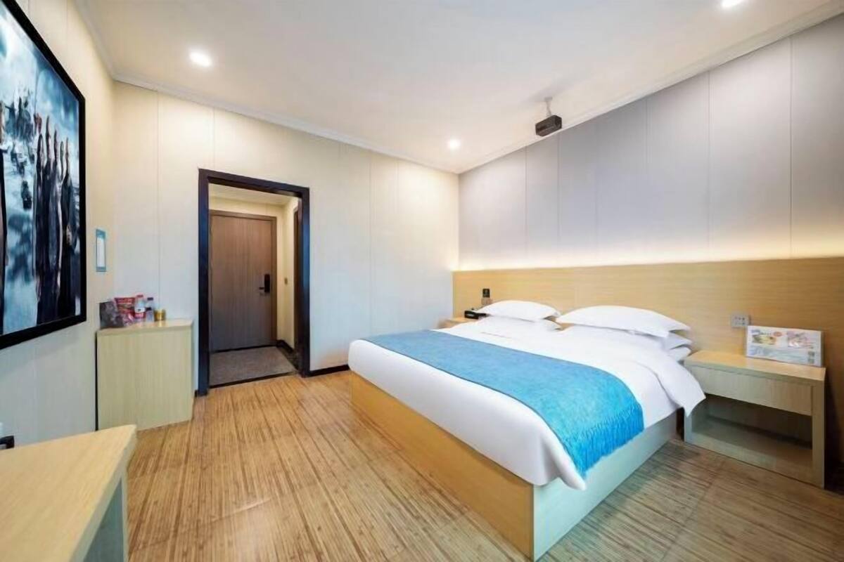 A hotel room with a bed, bedside table, and a door leading to another room.