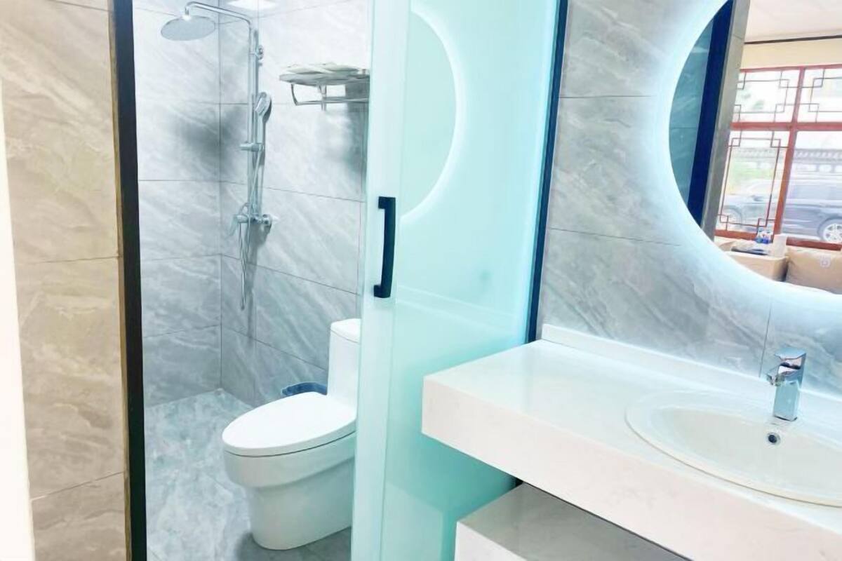 Ein modernes Badezimmer mit Duschkabine aus Glas, einer weißen Toilette und einem Waschtisch mit rundem Spiegel.