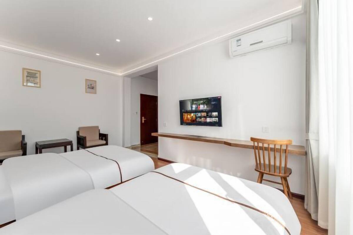 Ein modernes Hotelzimmer mit einem großen Bett, einem kleinen Schreibtisch, einem Sessel und einem an der Wand befestigten Fernseher.