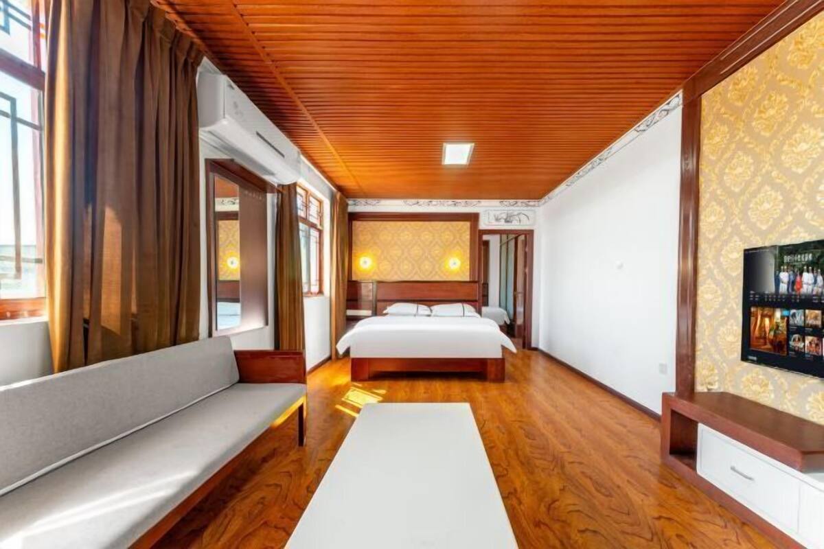 Ein Hotelzimmer mit Holzboden, einem großen Bett, einer Couch, einem Fernseher und Wandtapete mit Muster.