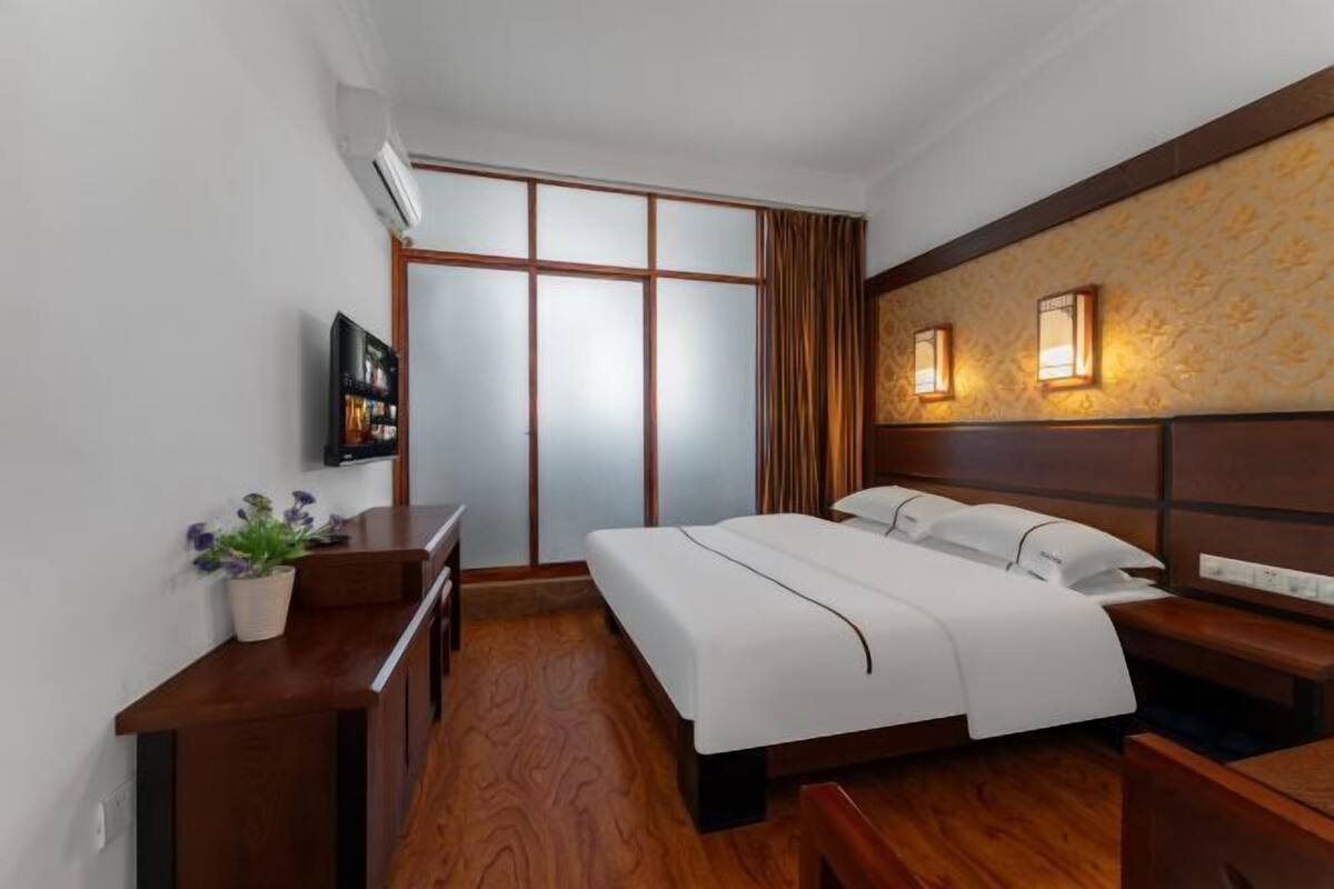 Ein Hotelzimmer mit Bett, Nachttisch, Fernseher und einer Wand-Klimaanlage.