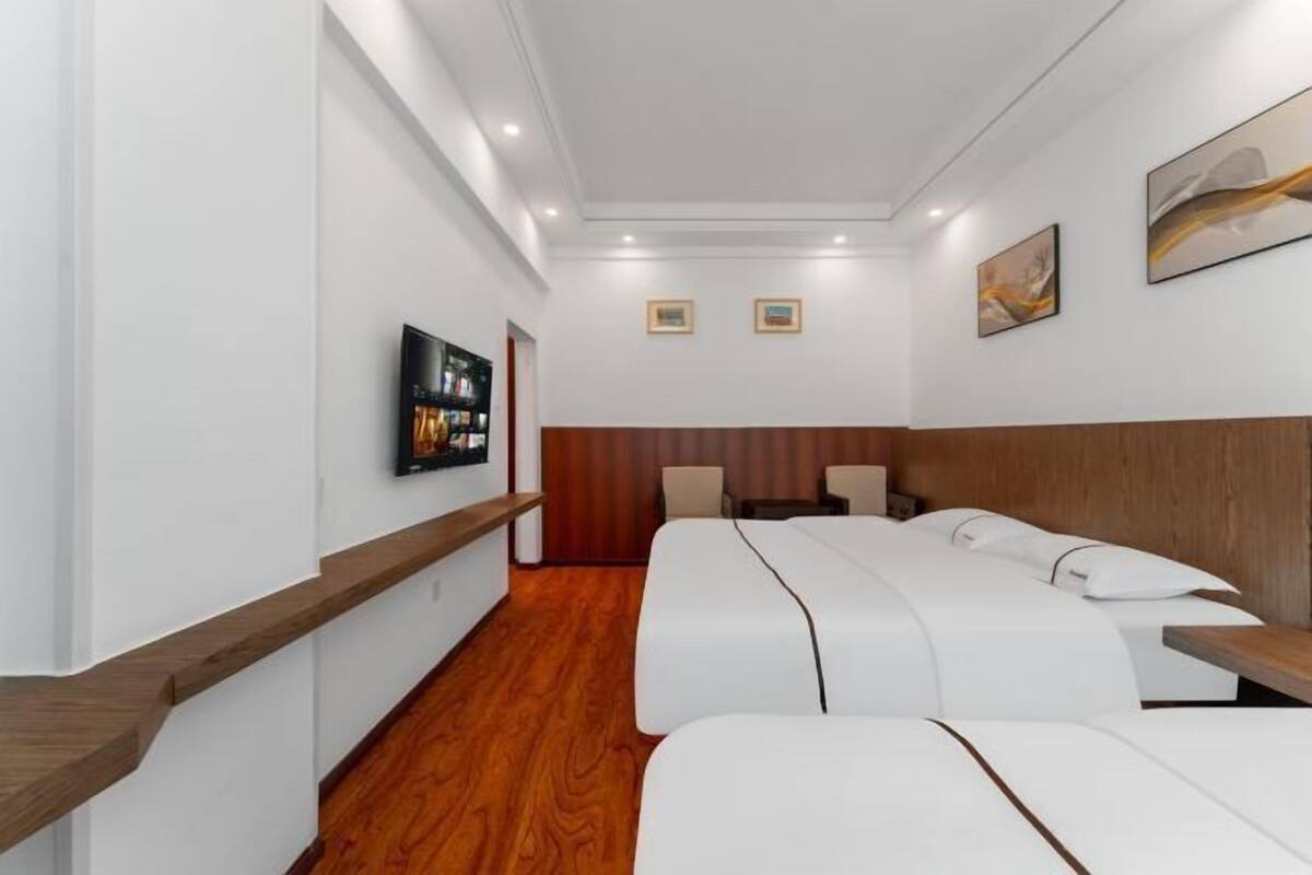 Ein Hotelzimmer mit Holzboden, weißen Wänden und einem hölzernen Kopfende. Es gibt zwei Betten mit weißer Bettwäsche und einen kleinen Tisch.