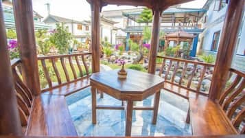 Un gazebo in legno con tavolo e sedie, circondato da un patio in pietra e un giardino con piante e un piccolo stagno.
