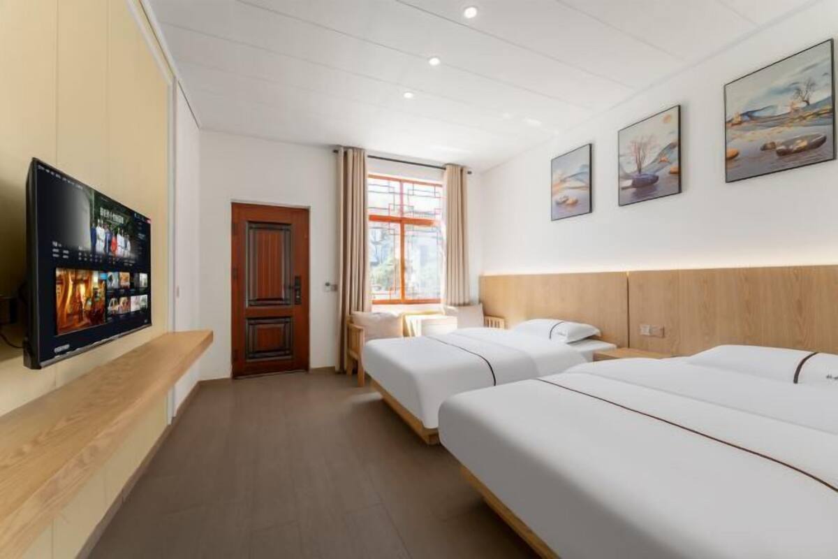 Ein Hotelzimmer mit zwei Betten, einem Wandfernseher, einem Schreibtisch und einem Fenster mit Vorhängen.