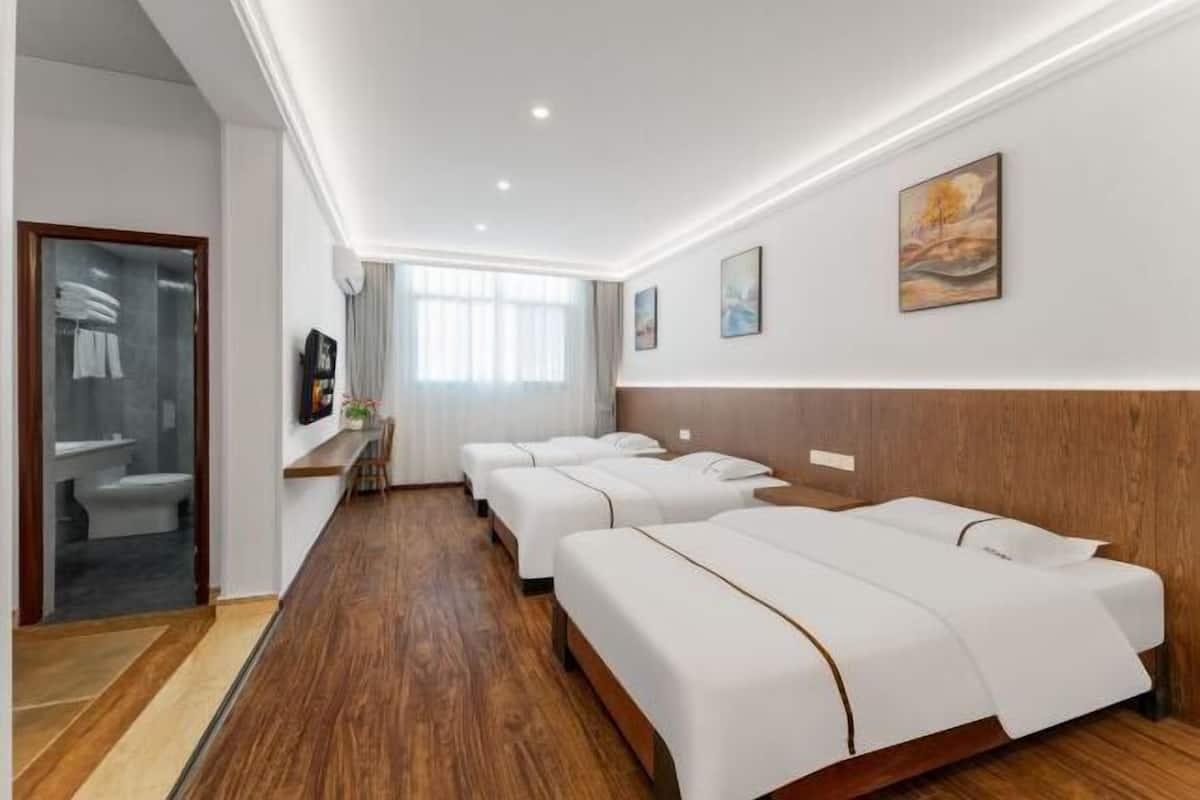 Ein Hotelzimmer mit vier Betten, Holzboden, einem Badezimmer mit Glastür und Kunstwerken an den Wänden.