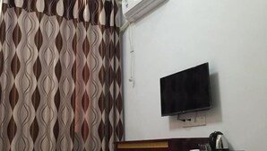 A hotel room with a patterned curtain, a flat-screen TV mounted on the wall, and a wooden side table with a kettle and a glass. - Qianyi Inn (Yichang)
