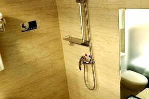 A shower with a handheld showerhead, a wall-mounted control panel, and a toilet visible through a partially open door.