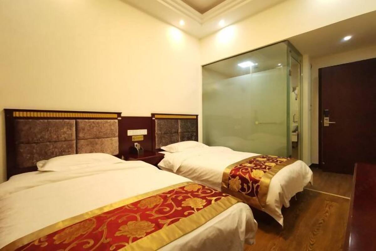 A hotel room with two beds, a glass shower enclosure, and a wooden floor.